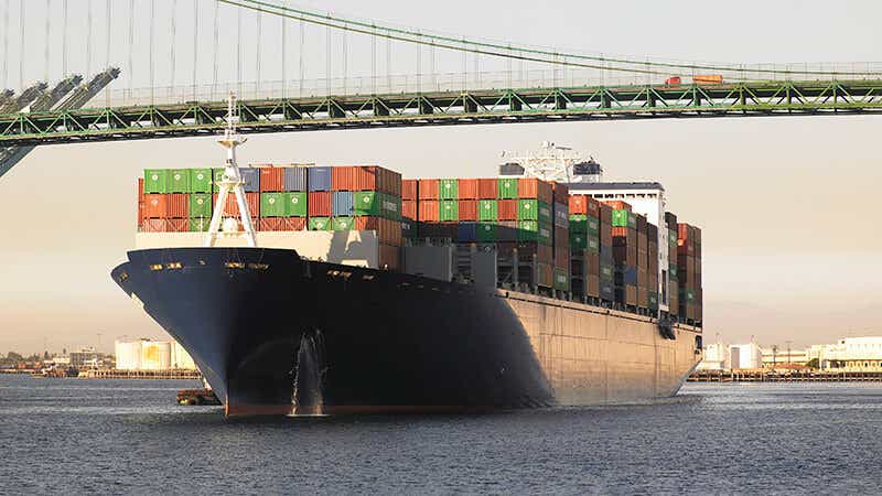 A cargo ship under a bridge transporting goods and materials.