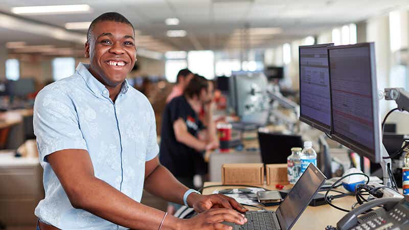 A freight broker standing in front of a computer and smiling.